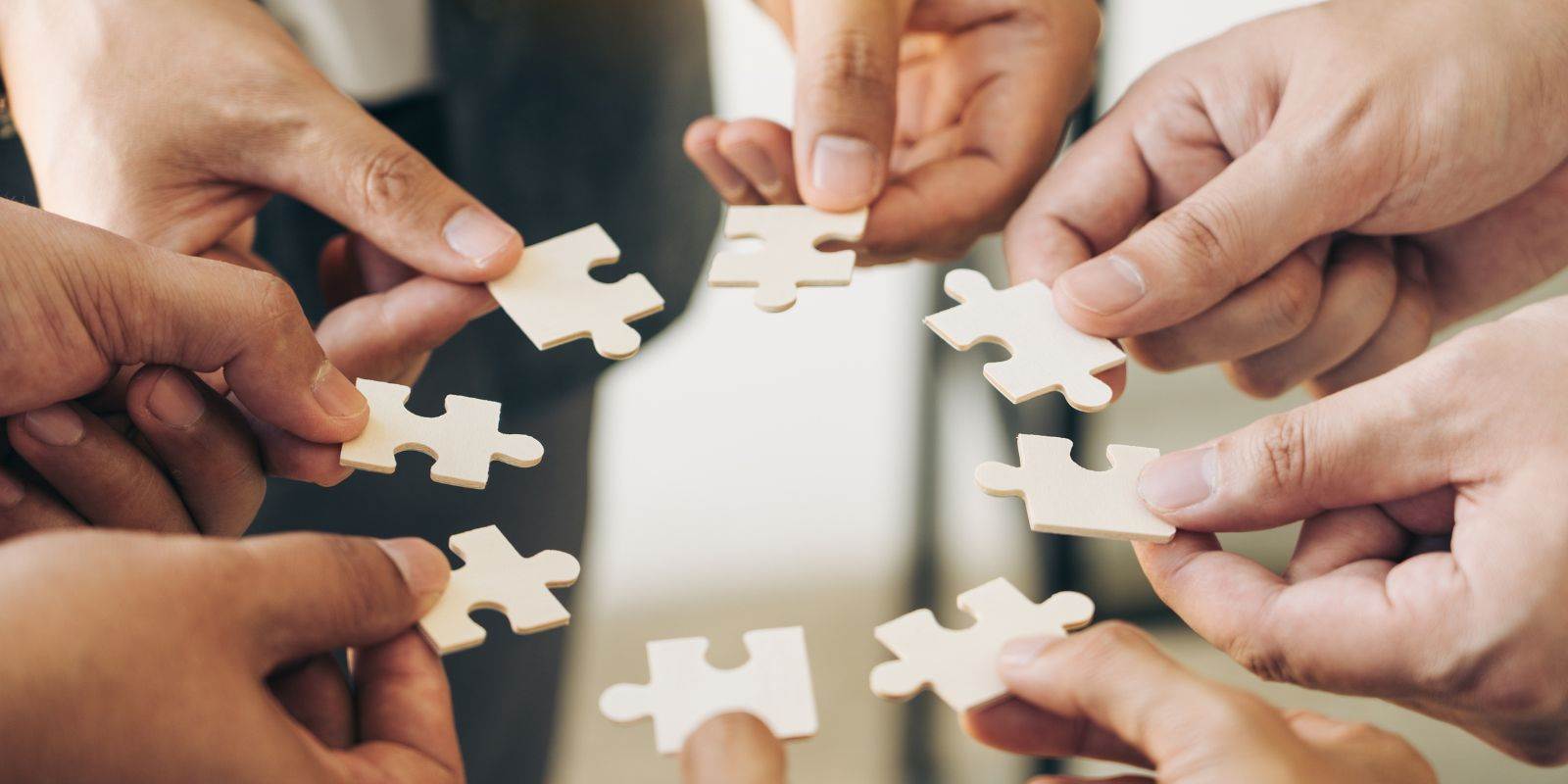 Hände die im Kreis zusammenkommen mit Puzzleteilen