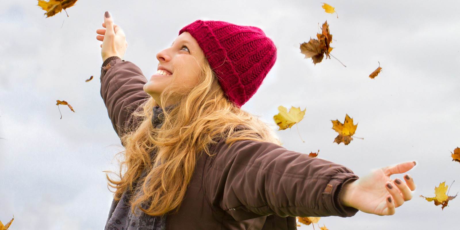 Lachende Frau mit herumwirbelnden Herbstblättern
