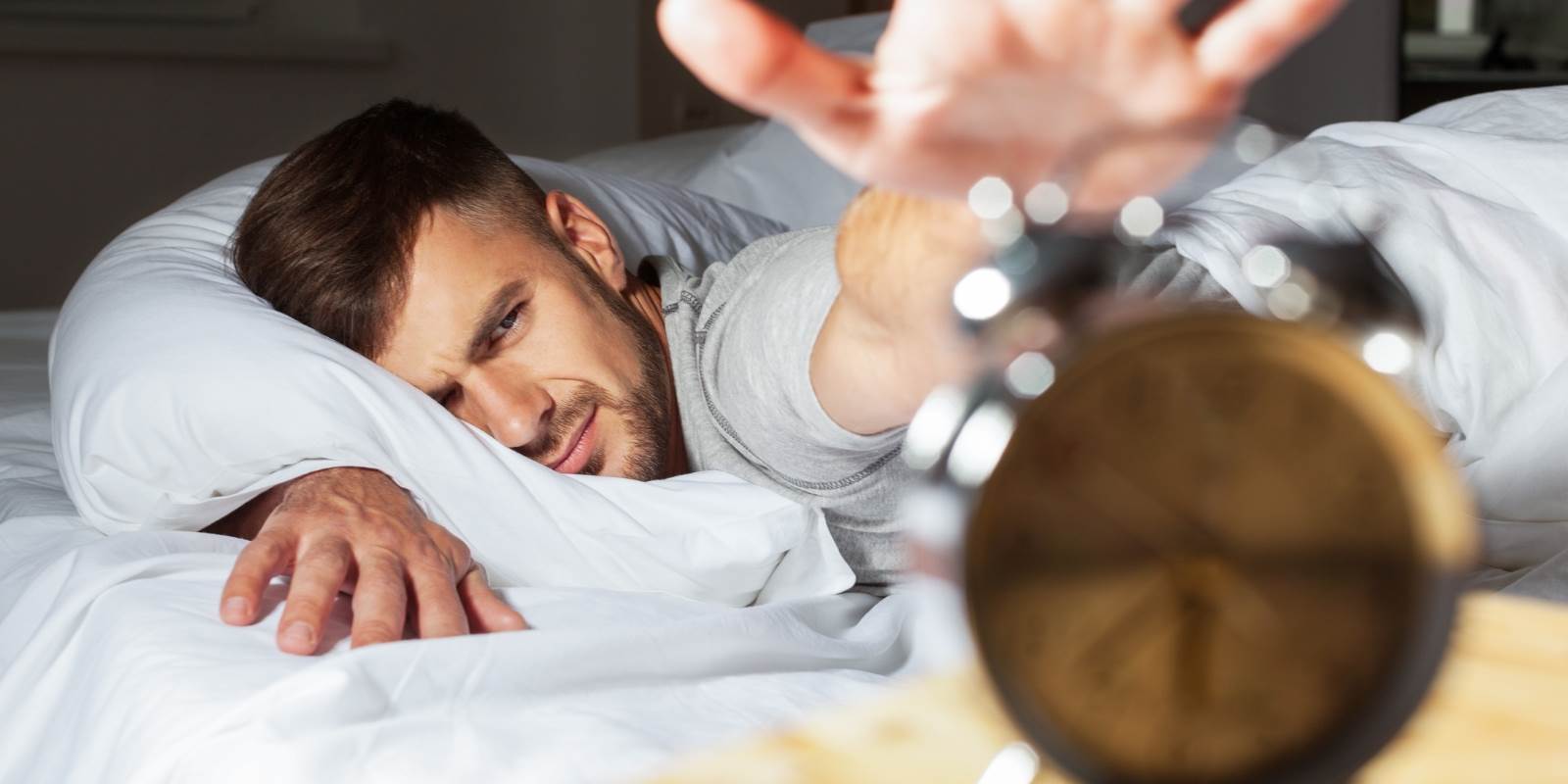 Mann schläft im Bett und stellt Wecker ab