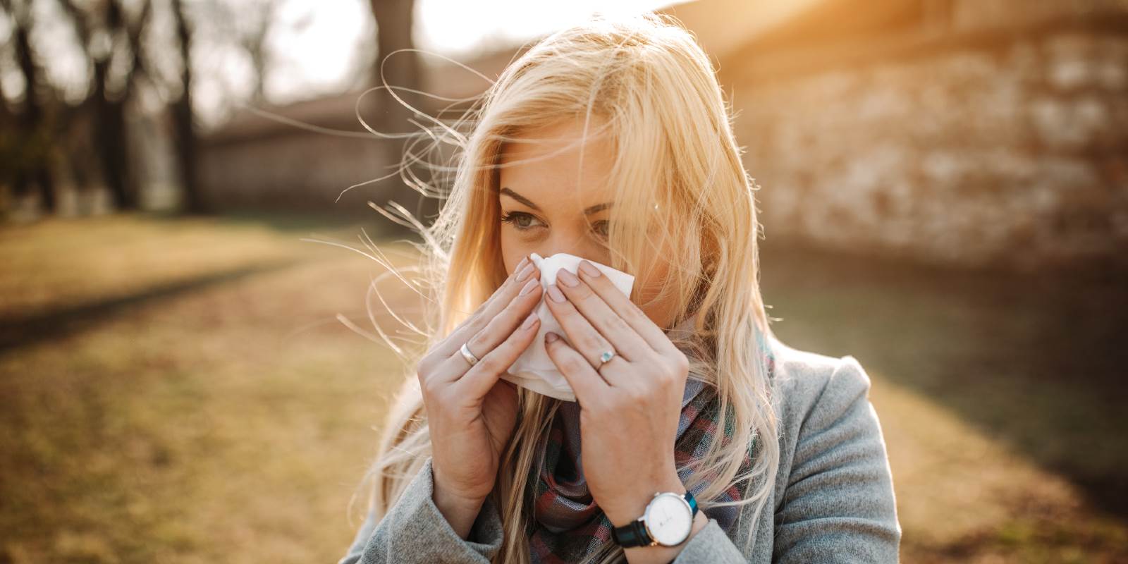 Frau mit grauer Jacke schnäuzt die Nase wegen Allergien.
